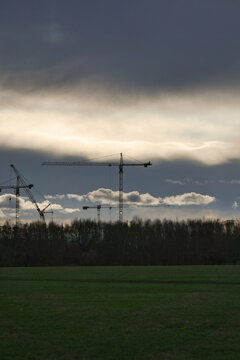 Construction Cranes Looming Over a Forested Landscape During a Dramatic Sunset