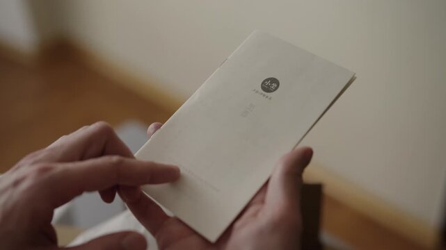 Ufa, Russia - 17 May 2026. Closeup of hands holding and opening small paper instruction manual with Asian text, leafing through pages to read product information, directions, warranty details indoors