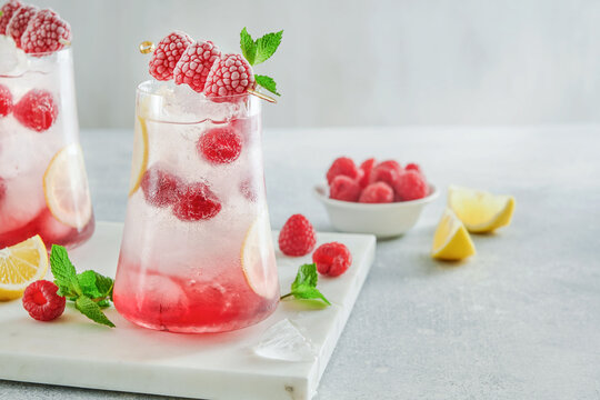 Refreshing raspberry iced drink with lemon slices, mint leaves, ice cubes and fresh berries on light table with copy space, summer beverage concept for mocktail recipe, lemonade menu, cafe promotion,