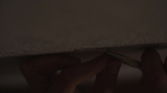 Anonymous person in dark room using pliers to extract hidden listening device or microchip from under surface. Concept of espionage, surveillance, secret operations, close-up, slow motion.