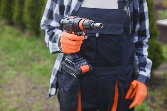 person holding power drill outdoors wearing orange gloves and black jacket for home improvement project in garden setting close-up practical and serene mood natural light clean background.