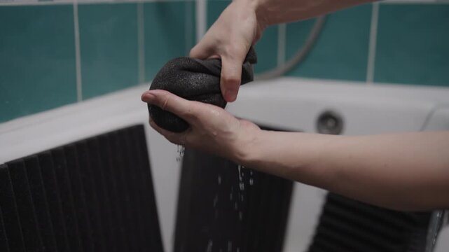 Close-up of male hands washing and wringing out black acoustic foam panels in bathtub. Squeezing water from soundproofing material for home studio or music room. DIY cleaning and preparation process.