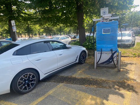 BMW i4 electric vehicle parked near wrapped FASTWAY charging station, Piazzale della Croce Rossa, Cremona, Italy