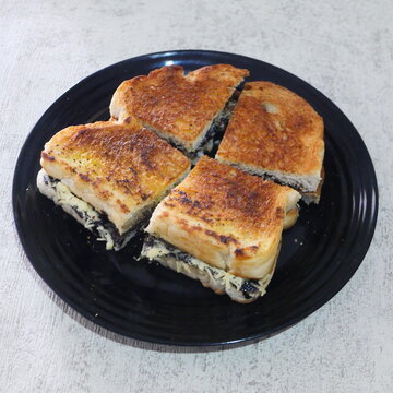 Chocolate and Cheese Grilled Bread (Roti Bakar) Cut into Four Pieces on a Black Plate