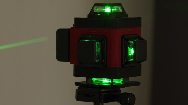 Close-up of a laser level with green lights glowing. Green laser beams project from the device. Red and black body is clearly visible. Ideal for construction alignment tasks