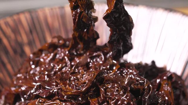Extreme close-up of metal chopstick,s lifting fresh, glossy raw seaweed from a bowl