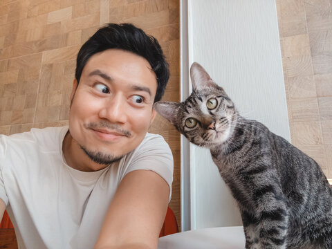 Funny Man Takes Selfie with Curious Tabby Cat, Sharing a Playful Moment Indoors