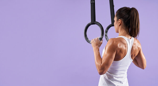 Woman gripping gymnastic rings, strong back muscles, intense workout, fitness training.