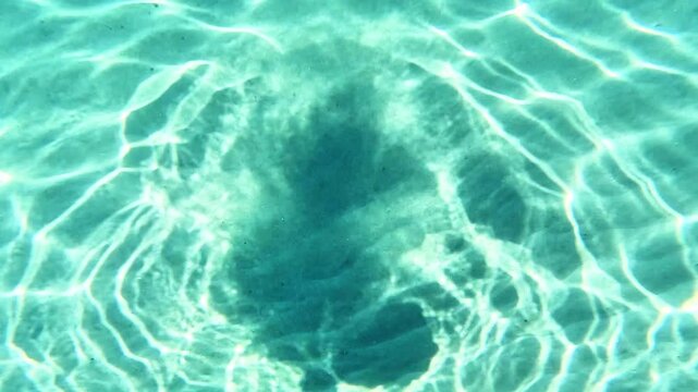 Swimming undersea POV near the sandy bottom illuminated by the sun's rays. The video was shot during a seaside holiday in Sicily, in the seaside village of Rodia
