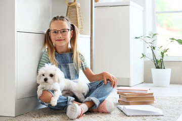 Obraz premium Cute little happy girl with Maltese dog and many books sitting on floor in kitchen