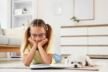 Obraz premium Cute little happy girl with Maltese dog reading book on floor at home