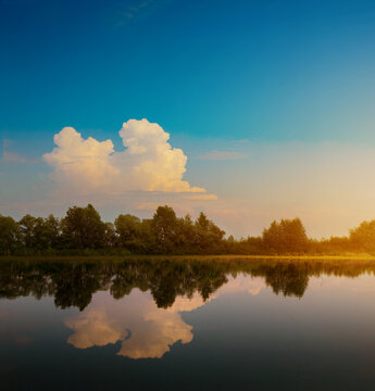 Still lake with mirror reflection of clouds and trees, calm summer landscape