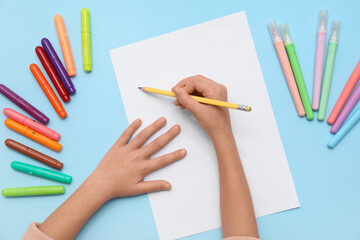 Naklejka premium Childs hands drawing with felt-tip pens and sheet of paper on blue background. Top view