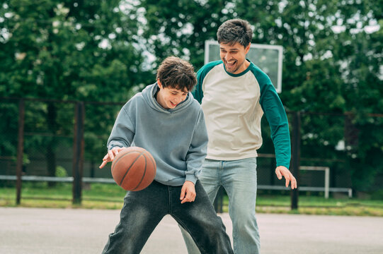 Teenage boy playing basketball outside with his father