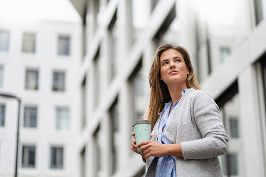 Young businesswoman with coffee to go cup, office building in the background