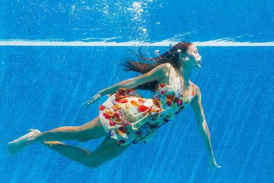 Woman in floral dress floating underwater in a swimming pool