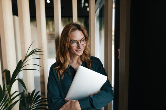 Smiling businesswoman holding laptop looking sideways