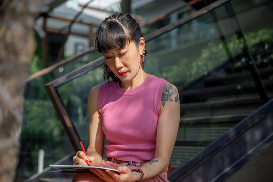 Woman drawing with pencil on sketch pad sitting in front of railing