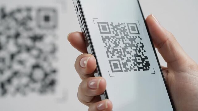 Close-up of a female hand scanning a QR code on a wall using a modern smartphone screen. Contactless payment, digital technology, and information reading concept.