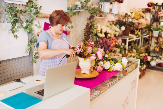 Mature female florist with brown hair using glue gun on flower pot while working in shop