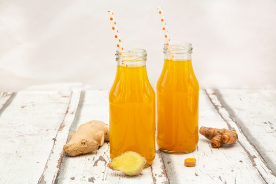 Ginger shot with orange and curcuma on white wood