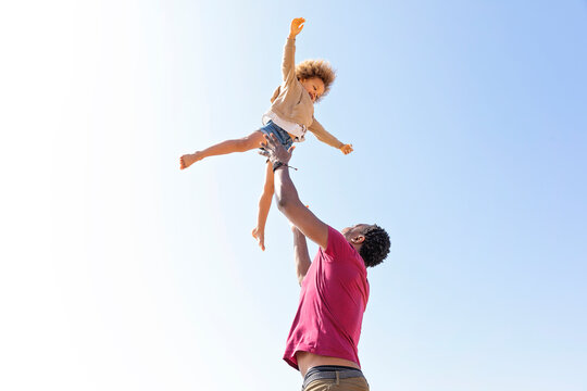 Playful father catching daughter under clear sky on sunny day