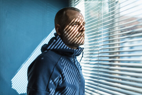 Pensive man looking out of venetian blind window
