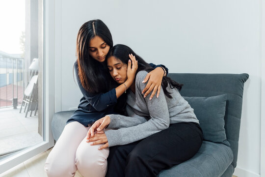 Young woman consoling sister on sofa in living room