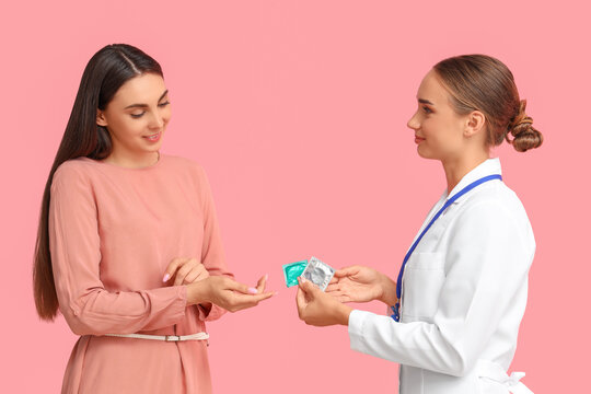 Female gynecologist giving condoms to patient on pink background