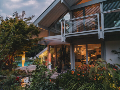 Illuminated modern timber frame villa with garden and pool at evening