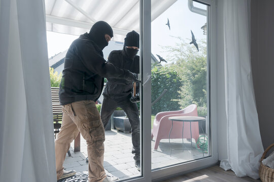 Two burglars opening terrace door of an one-family house with hammer and crowbar at daytime