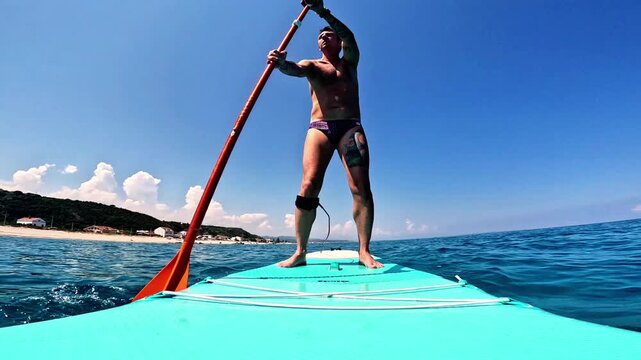 Slow-motion of a man who practices stand-up paddleboarding in the Mediterranean Sea along the coast of Sicily, the man is forty-two years old and of Caucasian origin
