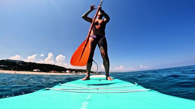 Slow-motion of a man who practices stand-up paddleboarding in the Mediterranean Sea along the coast of Sicily, the man is forty-two years old and of Caucasian origin