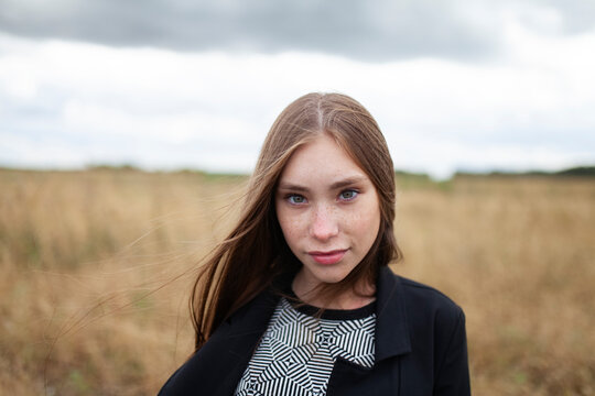 Female model with freckles stands in a dry summer field