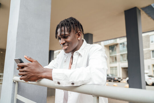 Smiling young man using mobile phone standing by railing
