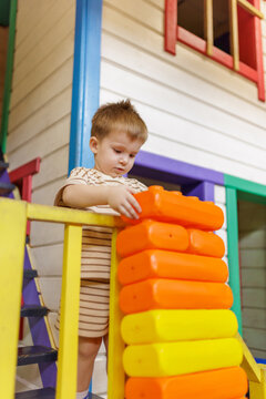 Cute little boy building tower from large plastic blocks on playhouse stairs