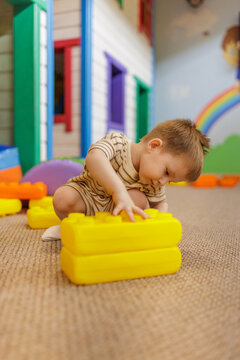 Cute little boy building with large yellow plastic blocks on playroom floor5