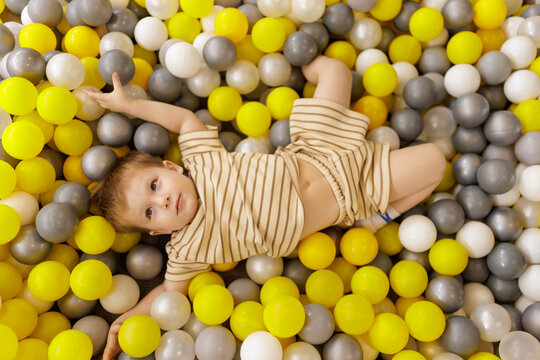 Cute little boy lying on back in ball pit at amusement center