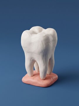 A handcrafted clay model of a molar tooth stands upright on a pink clay tongue base against a soft blue background, illustrating dental anatomy.