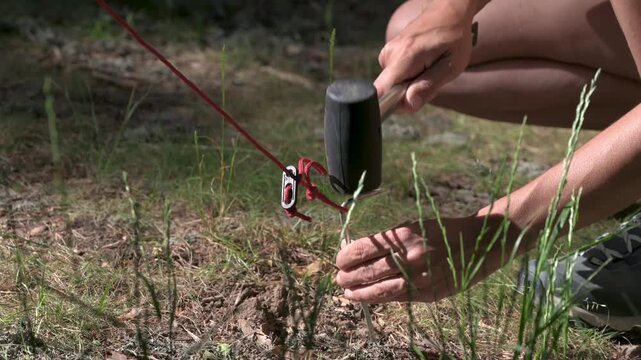 A person using a mallet to hammer a stake into the ground while camping