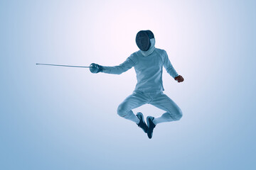 Fototapeta premium Male fencer jumping with epee during dynamic fencing action. Concept of explosive movement, athletic agility, sports performance, competitive fencing, and action photography.