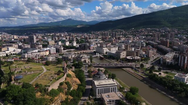 Wide panoramic drone overflight capturing the urban layout of Skopje, North Macedonia. Aerial perspective of the capital city valley nested under large green mountain ridges