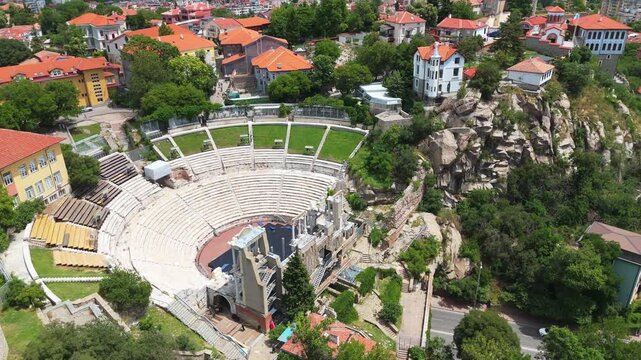 aerial drone view of the ancient Roman theater nestled among green trees and old houses in Plovdiv, Bulgaria. Beautiful historical preservation site from above.