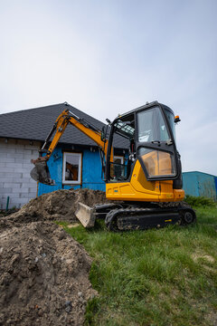 An excavator is digging near a house with blue walls while workers plan for an ongoing renovation project in the daytime