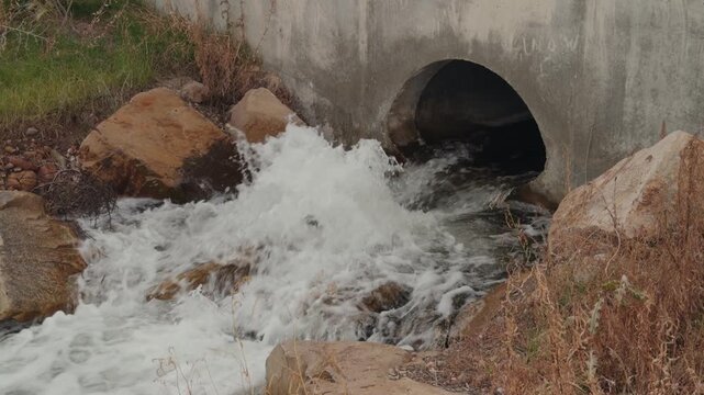 Water pours from a concrete drainage pipe into a rocky stream in slow motion