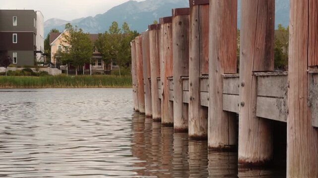 Row of weathered dock pilings stretches along a calm lake below mountains