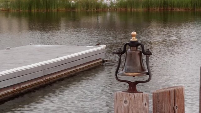 A weathered dock bell stands over a still lake as a bird flies past