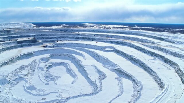 Huge industrial open pit mine with terraced slopes covered in snow, revealing its massive scale