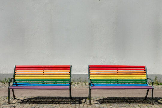 Colorful rainbow benches, LGBTQ+ pride flag colors in a street with copy space on a wall