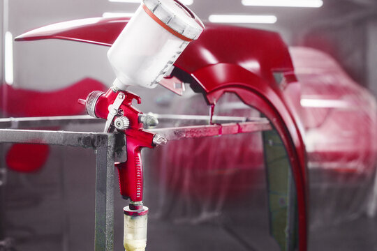 Airbrush gun in paint chamber on painted part car background. Painting of car body part in chamber with use airbrush gun.